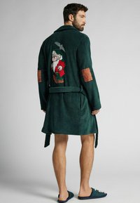 Zielona szlafrok z froty z haftowanym wzorem krasnala na plecach, związywany w talii, z brązowymi łatami na rękawach. W komplecie z pasującymi kapciami.