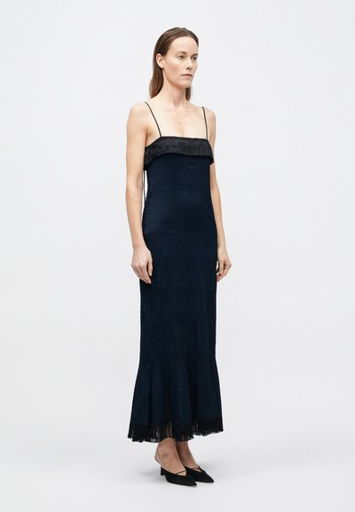 Sötétkék midi ruha, amelyen rojtos díszítés található a nyakkivágásnál, vékony pántokkal és bővülő szegéllyel. Simaságot és réteges részleteket kínál.