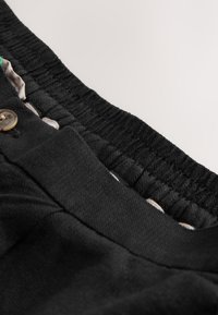Gros plan d'une ceinture élastique noire sur un pantalon avec bouton et doublure en tissu beige visible à l'intérieur.
