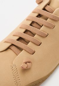 Barna sneaker sima, velúrszerű anyagból, lapos bézs fűzőkkel, csomós díszítéssel és oldalsó varrással.