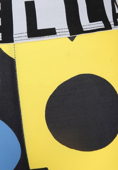 Leggings gialli con una texture costina, caratterizzati da grandi forme geometriche nere e blu, e una ampia cintura nera con testo.