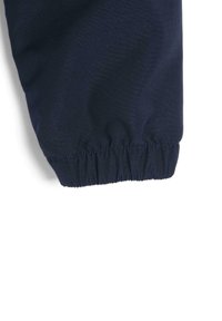 Poignet élastique bleu marine en tissu doux avec un léger éclat. Présente des coutures froncées pour un ajustement réglable au poignet.