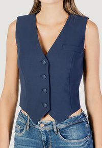 Gilet sans manches bleu marine avec un décolleté en V profond, cinq boutons et une petite poche poitrine. Ajustement cintré avec un ourlet angulaire. Tissu texturé.