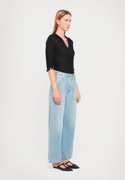 Black knit top with a V-neck and three-quarter sleeves, light blue high-waisted jeans, and black flat shoes. Frayed hem on sleeves.