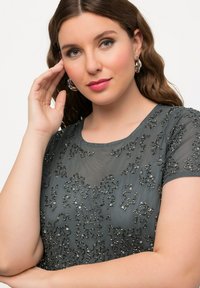 Šedý průhledný top s jemnými černými flitrovými detaily. Kulatý výstřih, krátké rukávy, měkká textura a volný střih.