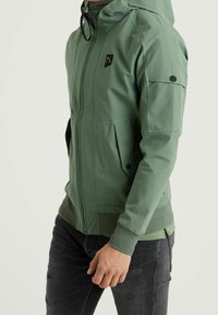 Green lightweight jacket with a hood, featuring a front zipper, side pockets, textured knit accent at the hem, and a logo on the chest.