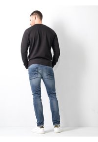 Sudadera negra de manga larga, jeans ajustados azules y zapatillas blancas. El conjunto presenta un diseño sencillo y un ajuste informal, con bolsillos en los jeans.