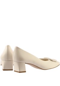 Zapatos de tacón de cuero blanco con punta cuadrada, que presentan un pequeño detalle de lazo en la parte delantera y un tacón grueso para mayor estabilidad.