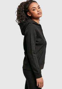 Czarna hoodie z przednią kieszenią, kapturem na sznurku i ściągaczami na rękawach. Charakteryzuje się prostym designem, bez wzorów i widocznych logo.