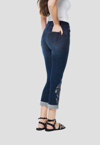 Sötétkék farmer capri nadrág felhajtott szegéllyel, színes hímzett virágmintákkal az oldalon és két hátsó zsebbel.