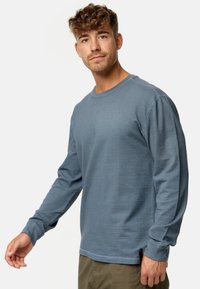 Langärmliges Hemd aus leichtem blauem, strukturiertem Stoff mit Rundhalsausschnitt. Verfügt über gerippte Bündchen und Schlitze an den Seiten für mehr Bewegungsfreiheit.