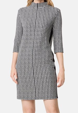 Black and white houndstooth knee-length dress with three-quarter sleeves and a high neckline worn by a standing person.