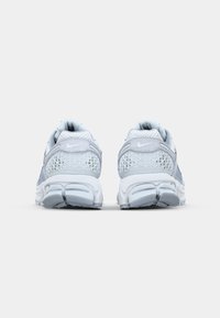 Tênis atléticos cinzentos e brancos com painéis de malha, parte traseira texturizada e amortecimento de calcanhar proeminente. Apresenta um design de sola curvada.