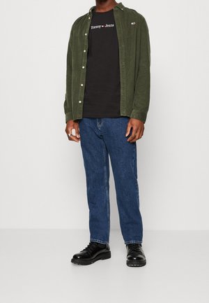 Green corduroy shirt over a black Tommy Jeans t-shirt, paired with blue jeans and black lace-up shoes. Features a relaxed fit and button details.