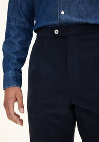 Denim shirt in dark blue with a button-down collar and two white buttons; paired with navy pants featuring flat front and side pockets.