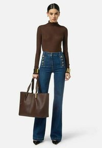 Dolcevita marrone, pantaloni a zampa di jeans blu a vita alta con dettagli di bottoni dorati e una borsa tote marrone testurizzata. Décolleté completano il look.