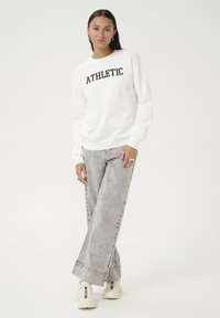 White sweatshirt with "ATHLETIC" in black lettering, paired with light gray wide-leg jeans and white sneakers.