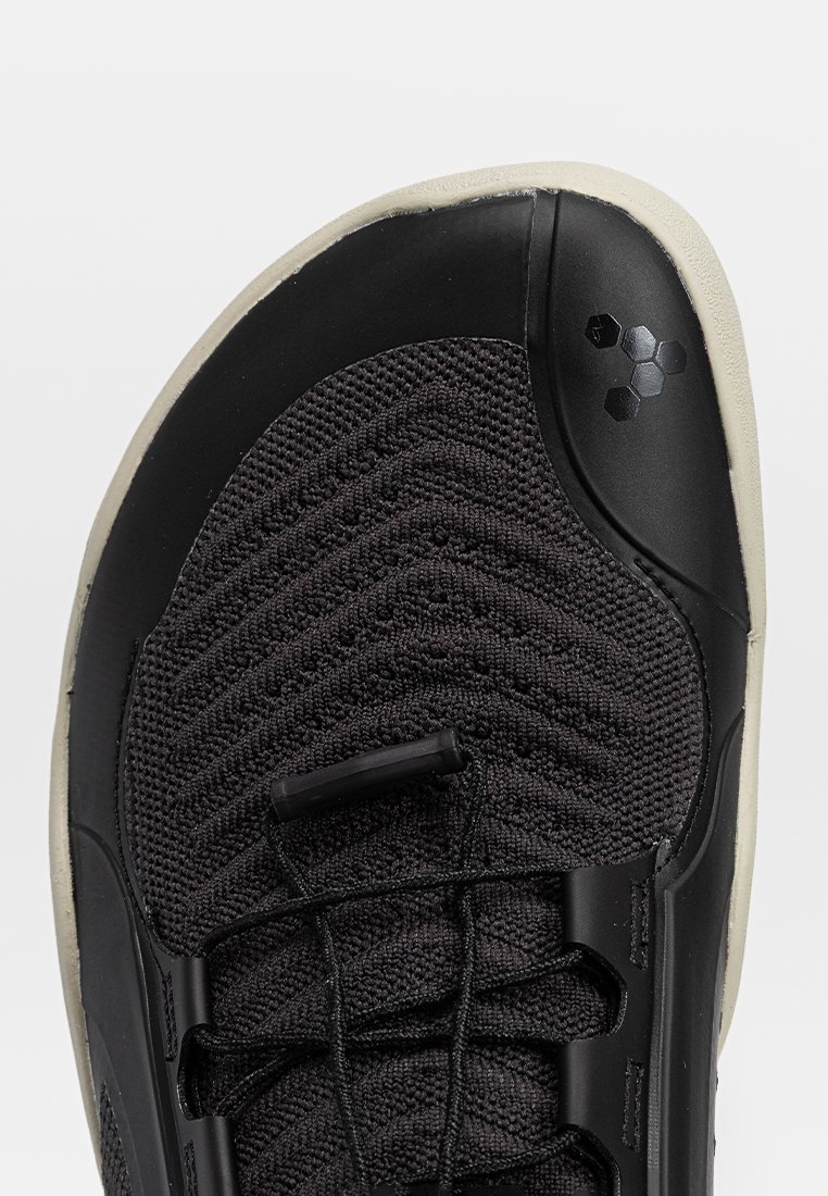 Schwarzer gestrickter Sportschuh mit beiger Sohle, schwarzem Kunststoff-Zehenkappe und schwarzen elastischen Schnürsenkeln mit Toggle-Verschluss.