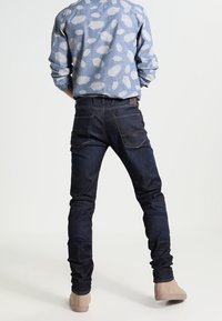 Tmavě modré džíny z denimu s úzkým střihem, kombinované se světle modrou košilí s listovým vzorem a béžovými kotníkovými botami.