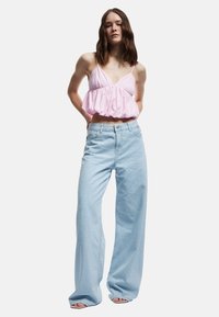 Vaaleanpunainen crop-top, jossa on säädettävät olkaimet, yhdistettynä vaaleansinisiin korkeavyötäröisiin farkkuihin, joissa on hieno kuosi ja leveät lahkeet.