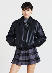 Giubbotto bomber in pelle sintetica nera con colletto ampio e chiusura con zip; abbinato a una gonna plissettata grigia a quadri con dettagli neri.