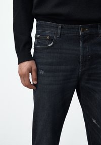 Mörkblå denimjeans med lätt blekningar, lätt slitningar och femfickorsdesign. Metalliska detaljer vid midjan och fickorna.