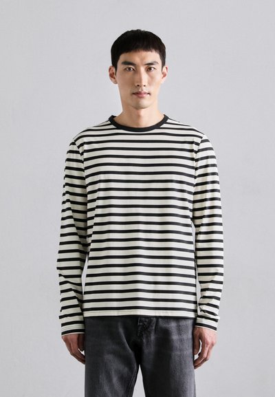 Chemise à manches longues avec des rayures horizontales noires et blanches, col rond et tissu doux, associée à un jean sombre.