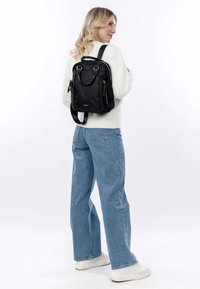 Black nylon backpack with dual shoulder straps, top handle, and zipped pockets. Smooth texture and minimalist design.