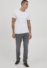 Camiseta blanca de manga corta combinada con jeans grises que presentan detalles desgastados. Zapatillas negras completan el conjunto.