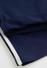 Tkanina w kolorze granatowym, gładka w dotyku, złożona z białym wykończeniem na dole. Prosty design, bez widocznych wzorów czy ozdób.