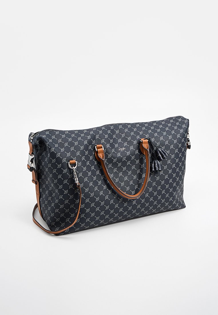 Dunkelblaue gemusterte Wochenendtasche mit braunen Ledergriffen, abnehmbarem Schultergurt und dekorativen Quasten auf weißem Hintergrund.