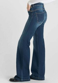 Jeans in denim blu a gamba larga, con vita media, caratterizzati da una texture liscia e un design accentuato delle tasche posteriori, con hardware dorato e cuciture in vista.