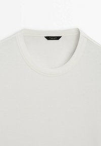 Hvid t-shirt med rund hals lavet af et glat stof. Har en syet krave og et mærke ved halsen med sort tekst.