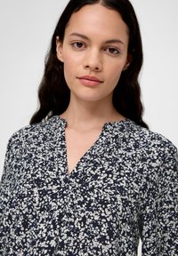 Navybluse mit einem weißen Blumenmuster, mit V-Ausschnitt und sanften Falten auf der Vorderseite. Leichtes Material mit weicher Textur.
