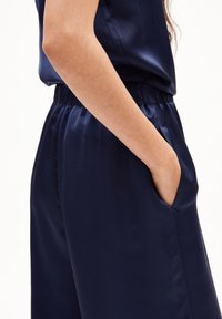 Marineblauer Satin-Overall mit lockerer Passform, elastischem Taillenbund und seitlichen Taschen. Glatte Textur mit dezentem Glanz.