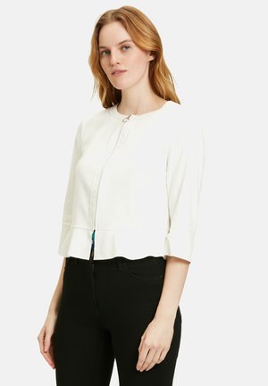 Giacca bianca corta con maniche a tre quarti, scollatura rotonda e zip frontale; presenta un lieve dettaglio peplum all'orlo.