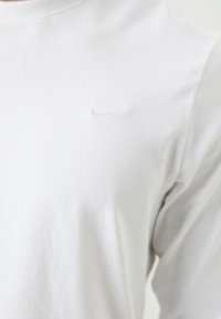 Hvid langærmet T-shirt lavet af bomuld. Har et lille, broderet Nike-logo på brystet. Glat tekstur, rund halsudskæring.