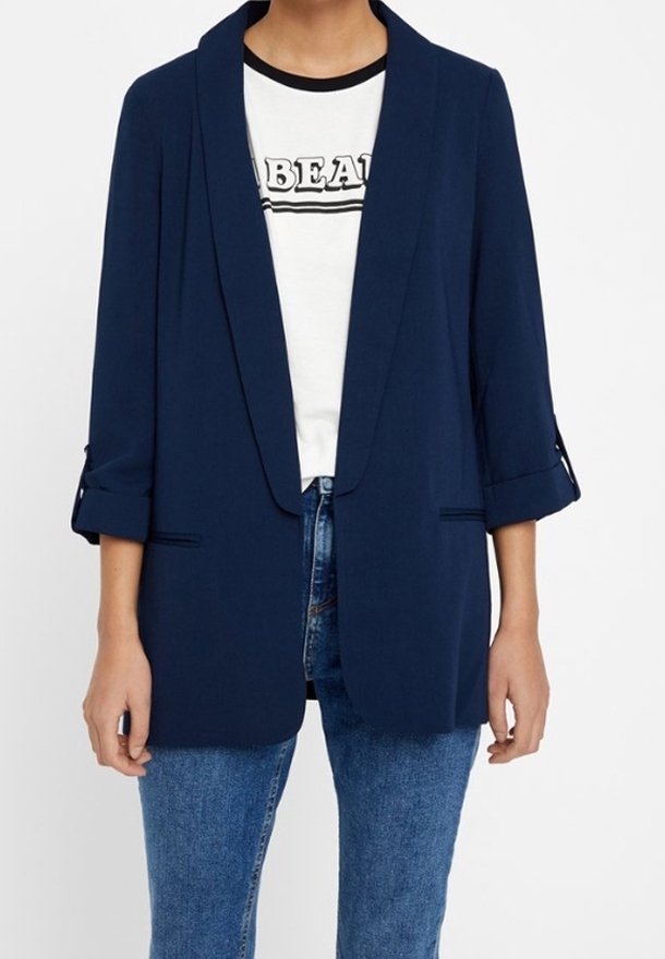 Granatowa marynarka z lekkiego materiału z kołnierzem szalowym, podwiniętymi rękawami i dwoma przednimi kieszeniami, noszona na koszulce z nadrukiem i dżinsach.