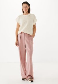 Cremefarbener gestrickter Oberteil mit kurzen Ärmeln, gepaart mit hoch geschnittenen, hellrosa weitem Bein Hosen. Die Schuhe haben ein braun-beige Design.