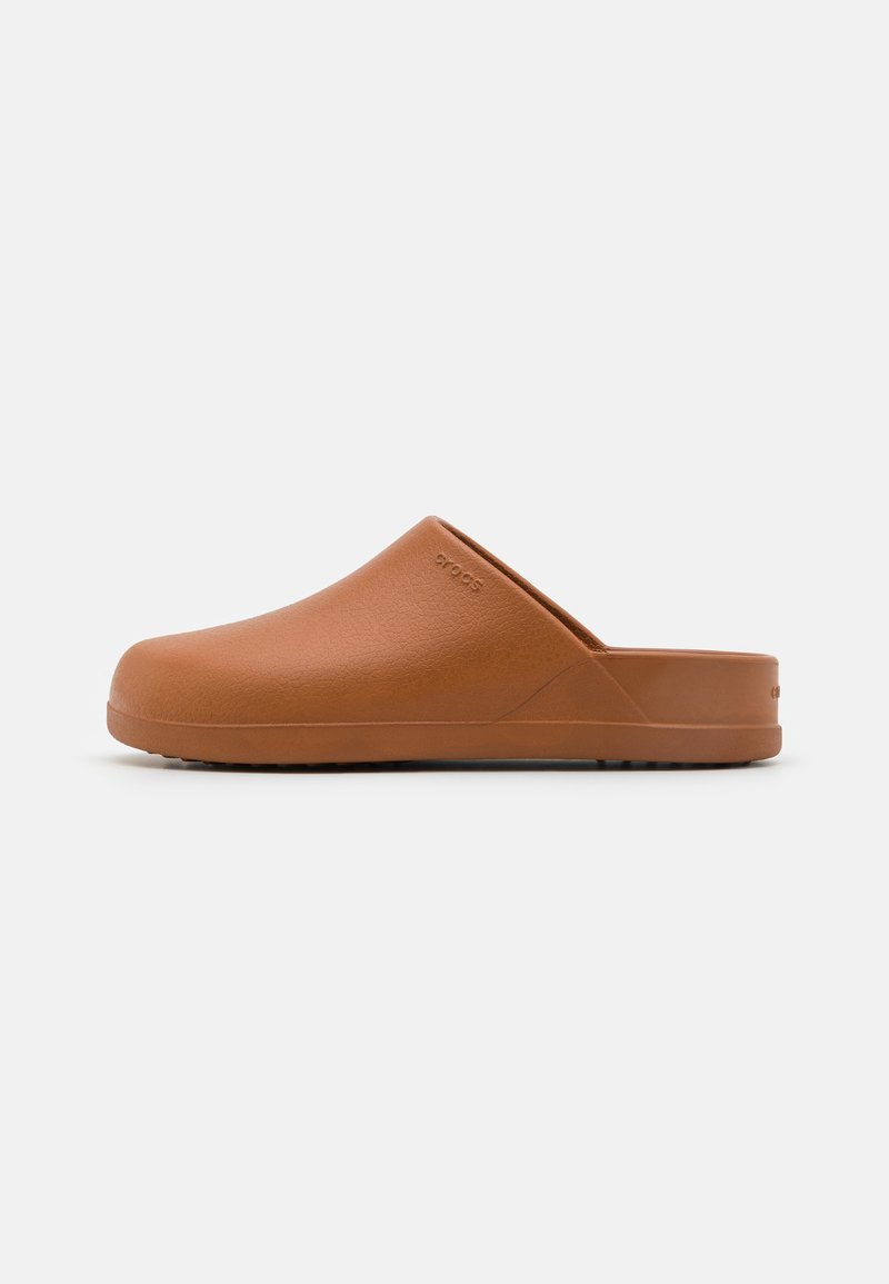 Sabot brun sans arrière avec bout fermé, talon bas, surface texturée et logo discret sur le côté, présenté sur un fond blanc uni.