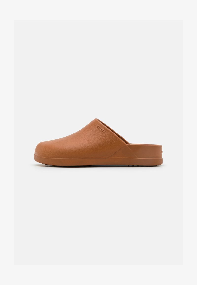 Sabot brun sans arrière avec bout fermé, talon bas, surface texturée et logo discret sur le côté, présenté sur un fond blanc uni.