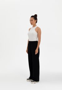 White ribbed tank top paired with black wide-leg pants and black-and-white sneakers. Simple, fitted design with an elastic waistband.