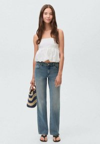 White strapless top with ruffled hem, light blue denim wide-leg jeans, and black sandals. Carrying a striped woven bag.