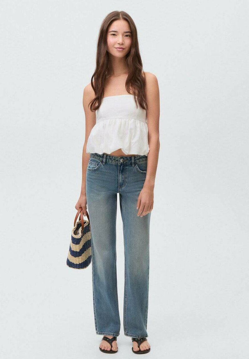 White strapless top with ruffled hem, light blue denim wide-leg jeans, and black sandals. Carrying a striped woven bag.