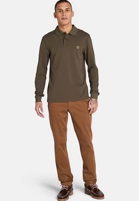 Långärmad olivgrön polotröja med krage, kombinerad med bruna byxor och bruna båtskor, med en logotyp på bröstet.