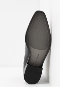 Suola di scarpe in pelle nera con una finitura liscia, dotata di uno strato di gomma testurizzata per grip, e un logo stampato vicino al tallone.