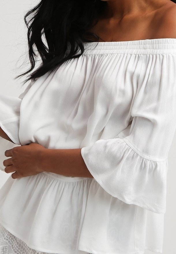 Bílý top s odhalenými rameny, krátkými rozšířenými rukávy a nařaseným pasem. Měkká, lehká tkanina s hladkou texturou.