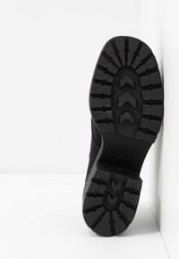 Semelle de chaussure noire en caoutchouc avec un motif de grip texturé. Vue latérale montrant un matériau supérieur lisse de couleur foncée, partiellement caché.