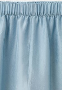 Jasnoniebieska zasłona z marszczonego materiału z widocznymi zagnieceniami i elastycznym górnym brzegiem do zawieszania.