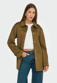 Brun mockajacka med krage, knappstängning och sidofickor, i kombination med en åtsittande vit topp och jeans.
